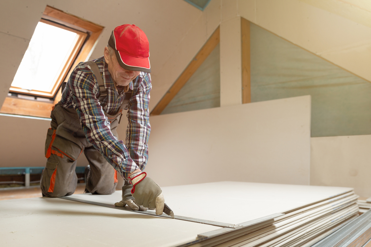 Worker cutting drywall plasterboard with construction knife. Attic renovation